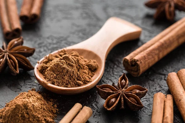 ground cinnamon spice powder in wooden spoon, on dark concrete background.  Cinnamon, whole sticks  with a heap of powder.  Ingredients for cooking. Banners of herbs and spices. Space for text