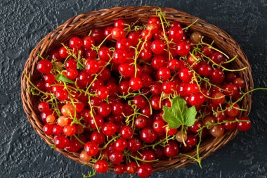 Siyah taş zemin üzerine bir hasır sepet meyveleri taze sulu kırmızı kuş üzümü. Yaz hasat. Sağlıklı beslenme kavramı