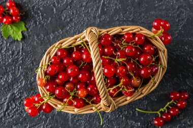 Siyah taş zemin üzerine bir hasır sepet meyveleri taze sulu kırmızı kuş üzümü. Yaz hasat. Sağlıklı beslenme kavramı