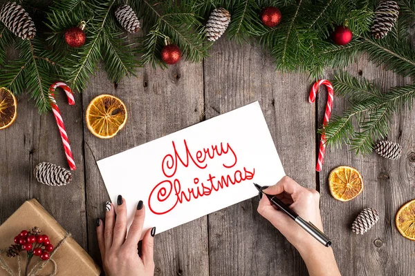 Merry Christmas hand lettering inscription on old wooden background. Pine branches and cones frame. New Year and Christmas celebration. Winter holidays concept. Christmas decorations. Top View