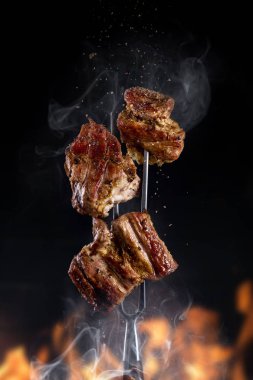 Siyah arka planda lezzetli ızgara et parçaları olan çatal.