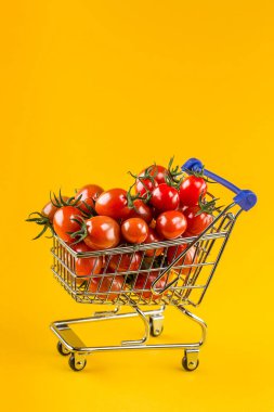 Sarı arka planda alışveriş arabasında sulu domatesler