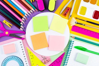 Okul konseptine geri dönelim. Renkli kağıt arkaplanda çeşitli yazma araçları.