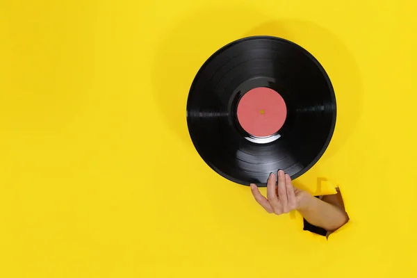 Női kéz tartja Vinyl Record keresztül szakadt lyuk a sárga papír fal — Stock Fotó