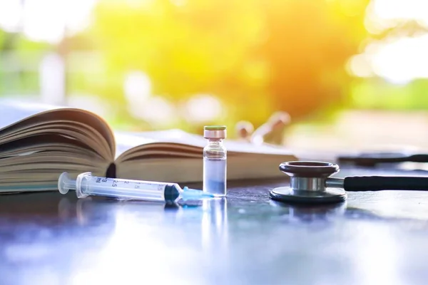 Masada şırınga iğnesi, steteskop ve tıp kitabı, enjeksiyon tedavisi için tıbbi konsept enjeksiyon tedavide hastalık teşhisi, mavi ışık arka planı, seçici odaklanma