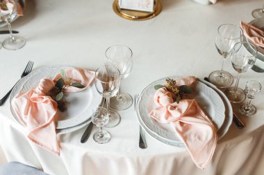 Kutlama masasını boş şarap bardakları ve iki tabakla kapatın. Beyaz tabaklar, pembe peçete ve şarap kadehleri ile kutlama ziyafeti. Restorandaki beyaz ve kırmızı masada.