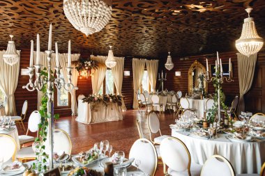 Boş şarap kadehleri ve mumlarla dolu üç şenlik masa. Beyaz peçeteli, beyaz tabaklı ve şarap kadehli kutlama ziyafeti. Restorandaki beyaz masada beyaz ve kırmızı şarap.