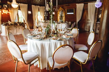 Boş şarap kadehleri ve mumlarla dolu üç tane düğün masası. Beyaz peçeteli, beyaz tabaklı ve şarap kadehli kutlama ziyafeti. Restorandaki beyaz masada beyaz ve kırmızı şarap.