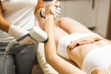 Güzellik salonunda lazer epilasyonu ve kozmetoloji. Saç çıkarma prosedürü. Lazer epilasyonu, kozmetoloji, spa ve saç temizleme konsepti. Güzel bir kadın ellerindeki kılları aldırıyor.