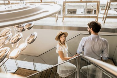 Restorantın merdivenlerinde şık bir çift. Yukarıda mutlu bir aile ve kameraya bakan beyaz şapkalı bir kadın.