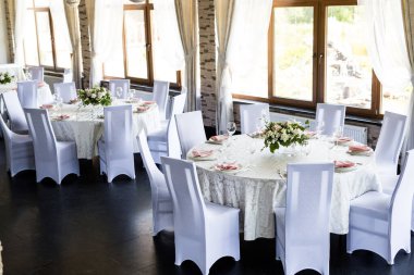 Şarap kadehleri ve taze çiçeklerle dolu iki şenlikli masa. Restoranda pembe peçeteler, beyaz tabaklar ve şarap kadehleriyle kutlama ziyafeti