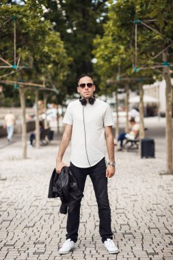 Boynunda kulaklıkla gülümseyen adam, kameraya bak. Siyah gözlüklü ve beyaz tişörtlü DJ.