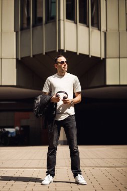 Elinde kulaklıkla gülümseyen adam, başka yere bak. Siyah gözlüklü ve beyaz tişörtlü Dj bina arka planında