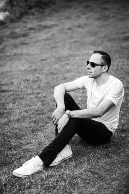 Gülümseyen bir adamın dikey fotoğrafı yeşil çimlerde oturur ve başka yere bakar. Doğada DJ 'in siyah beyaz fotoğrafı