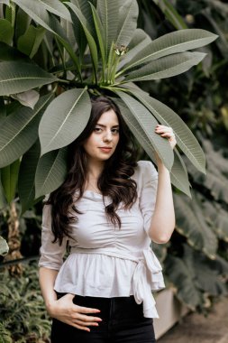 Kamerada beyaz bluz ve siyah pantolon giyen çekici bir kadının portresi var. Doğası gereği genç bir kadın.