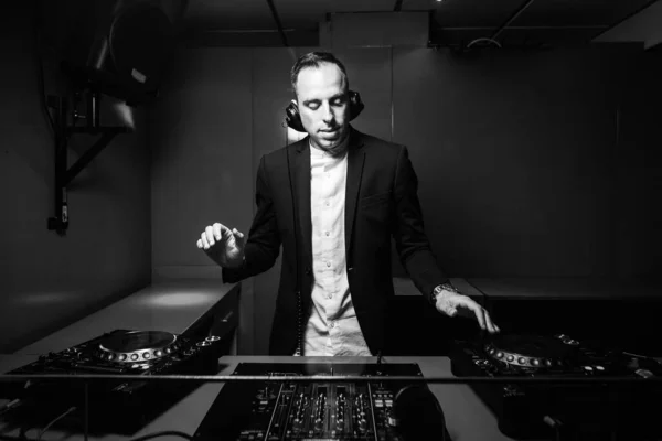 DJ with headphones at night club party. Black and white photo of man in black suit playing music on deck with vinyl record