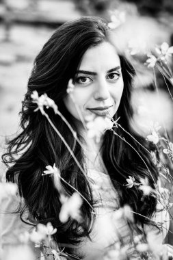 Etrafı çiçeklerle çevrili güzel bir genç kadının siyah beyaz fotoğrafı. Çiçek arkaplanda esmer bir kadın