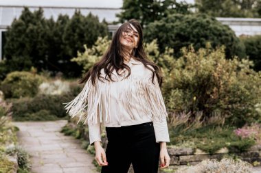 Bej renkli ceket giyen, gülümseyen çekici bir kadın ve dışarı bakan bir kamera. Doğada yaşayan genç bir kadın