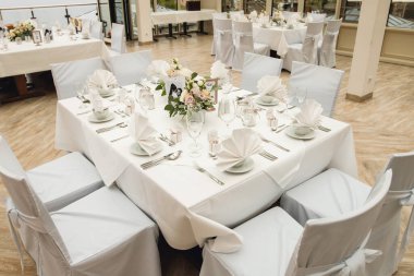 Şarap kadehleri ve taze çiçeklerle süslenmiş şenlikli masa manzarası. Restoranda beyaz peçeteler, beyaz tabaklar ve şarap kadehleriyle kutlama ziyafeti