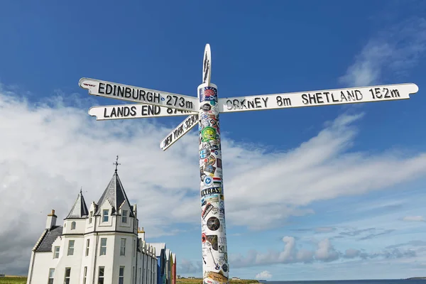 Les Britanniques débarquent en signe d'extrémité aux toilettes O'Groats en Écosse avec le ciel bleu et l'océan et l'herbe en arrière-plan. A beaucoup d'autocollants sur le poste . — Photo