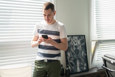 Genç adam işadamı pencerenin yanında duruyor, ofisteki telefona bakıyor.