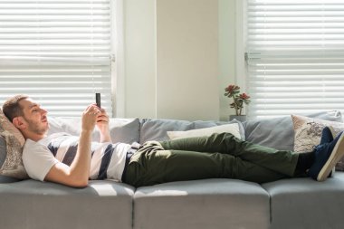 Yakışıklı genç adam akıllı telefonuna bakarken, evde kanepede yatarken