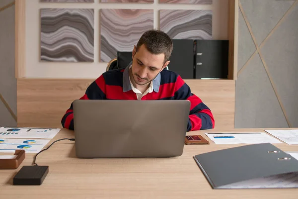 Jovem homem de negócios trabalhando em um laptop em sua mesa no escritório — Fotografia de Stock