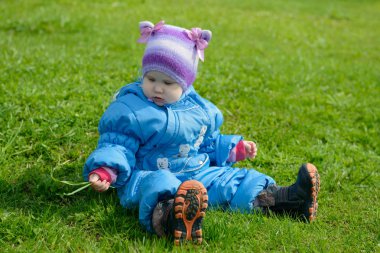 küçük çocuk bir mavi tulum içinde yeşil çimenlerin üzerinde oturur ve bir bıçak çimen inceliyor