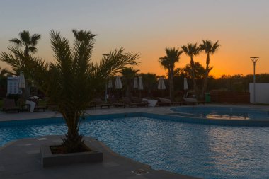 Şezlong ve şemsiye gün batımında Yüzme Havuzu