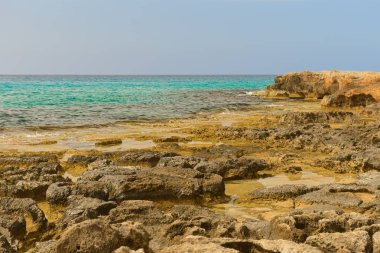 Turkuaz su ve mavi gökyüzü ile kayalık deniz kıyısı