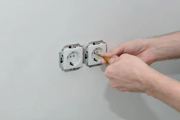 hands of an electrician install sockets on a white wall