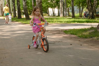 Küçük kız parkta bir çocuk dört tekerlekli bisiklet sürmek