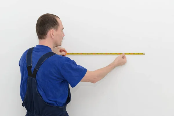 Worker in overalls measures the distance on a white wall using a — 스톡 사진