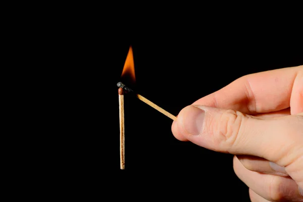 Une main avec un match allumé met le feu à un nouveau match sur un dos noir — Photo