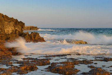 Kayalık bir kıyısı ve dalgaları olan deniz akşamı manzarası