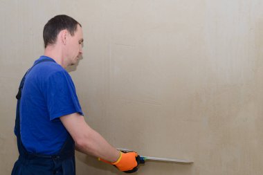 Tulumlu bir alçı duvara beyaz macun koyuyor.