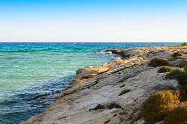 Güneşli bir akşamda mavi denizde kayalık bir plaj.