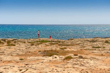 2 Mayıs 2014: Genç bir çift kayalık bir sahilde yürür ve fotoğraf çeker. Kıbrıs.