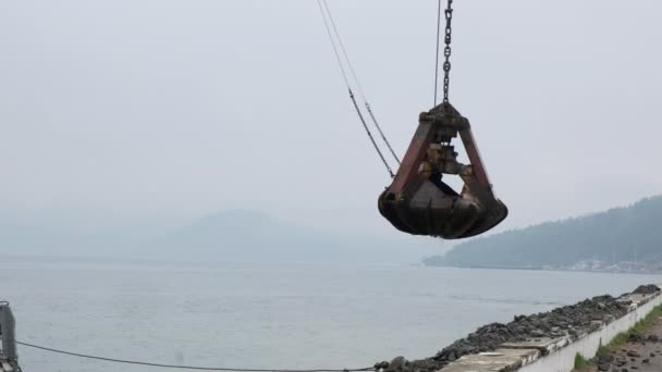 Une grue à benne preneuse sur une plate-forme flottante travaille sur le remplissage et le renforcement de la rive du lac Baïkal avec de grandes pierres — Video