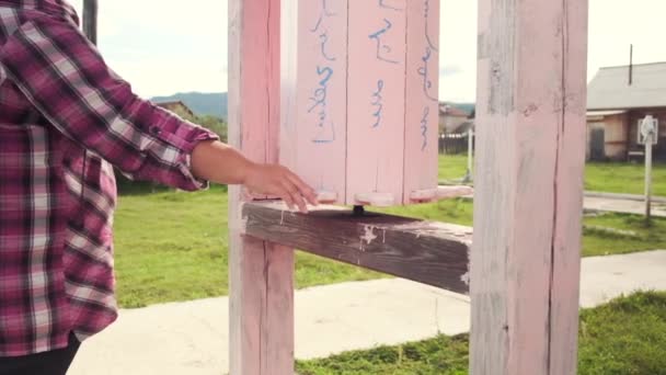 Βίντεο αργής κίνησης ενός κοριτσιού που περιστρέφεται ξύλινα ροζ τύμπανα κοντά σε έναν βουδιστικό ναό κατά τη διάρκεια της προσευχής — Αρχείο Βίντεο