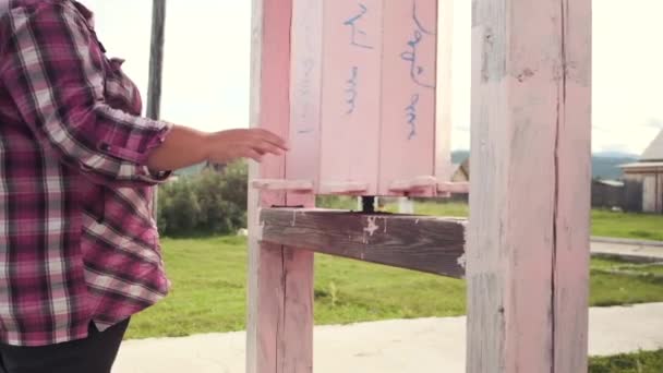 Video al rallentatore di una ragazza che ruota tamburi rosa di legno vicino a un tempio buddista durante la preghiera — Video Stock