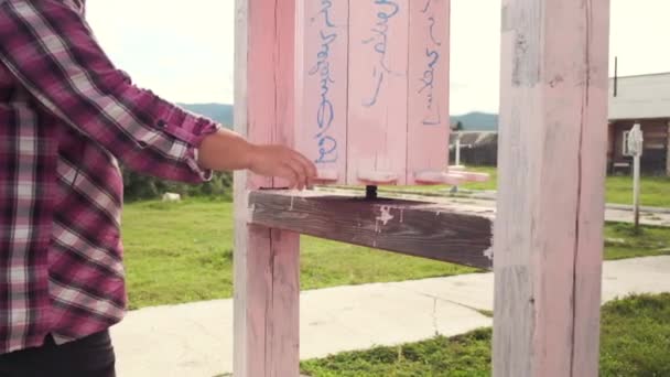 Slow motion video van een meisje roterende houten roze drums in de buurt van een boeddhistische tempel tijdens gebed — Stockvideo