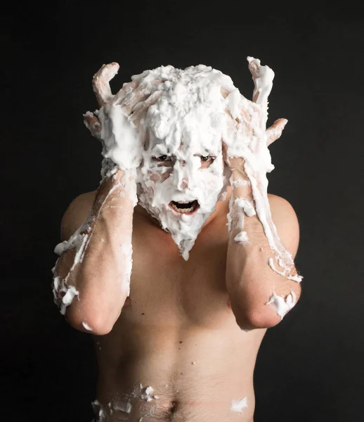 photo portrait of a muscular screaming man smeared with shaving foam with hands on his head like the horns of a buffalo