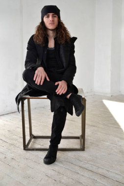 uzun kıvırcık saçlı siyah giysiler ve bir kap masaya oturur