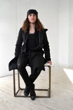 Fotoğraf adam siyah giysiler ve bir kap uzun kıvırcık saçlı masaya oturur