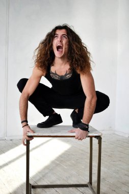 Fotoğraf adam siyah giysili uzun kıvırcık saçlı bir tabure gibi bir vahşi ve çığlıklar üzerine tırmandı