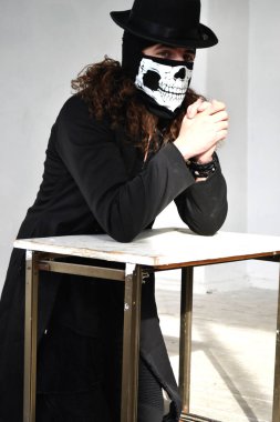 Fotoğraf portre siyah giysili uzun kıvırcık saç ve bir şapka onun yüz dua üzerinde bir kafatası şeklinde maskeli bir adam