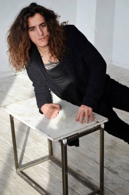 Fotoğraf üzgün adam siyah giysili uzun kıvırcık saçlı masanın üzerine eğildi