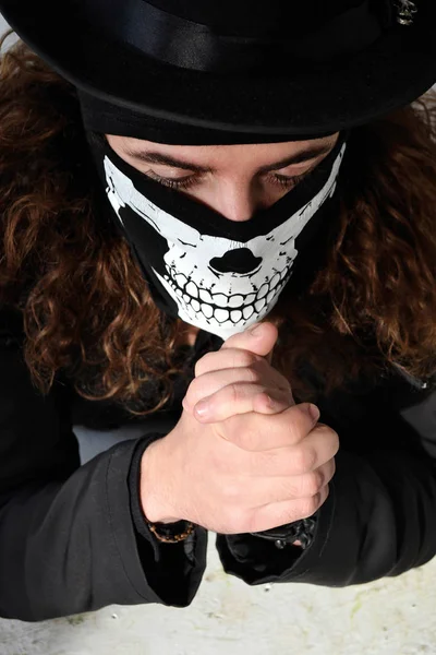 siyah giysili uzun kıvırcık saç ve bir şapka onun yüz dua üzerinde bir kafatası şeklinde maskeli bir adam portresi fotoğraf