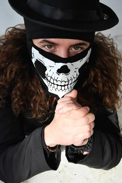 uzun kıvırcık saç siyah giysili ve bir şapka onun yüzünde bir kafatası şeklinde maskeli bir adam portresi fotoğraf